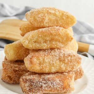 stack of several air fryer churros with cinnamon sugar coating on a white plate.