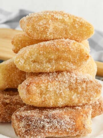 stack of several air fryer churros with cinnamon sugar coating on a white plate.