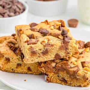 three peanut butter cup cookie bars stacked on a white plate.