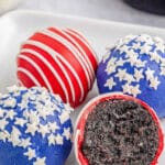 four red and blue coated Oreo balls with candy star and stripes on a white plate.