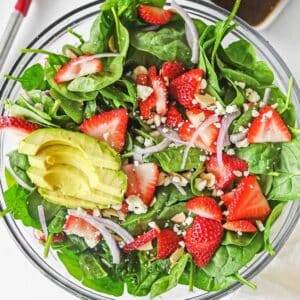 Large glass bowl of strawberry spinach salad ingredients mixed together.