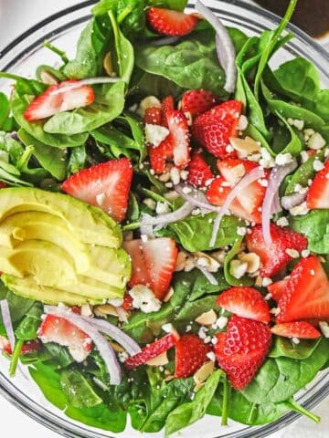 Large glass bowl of strawberry spinach salad ingredients mixed together.