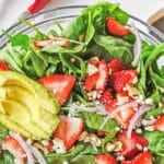 Large glass bowl of strawberry spinach salad ingredients mixed together.