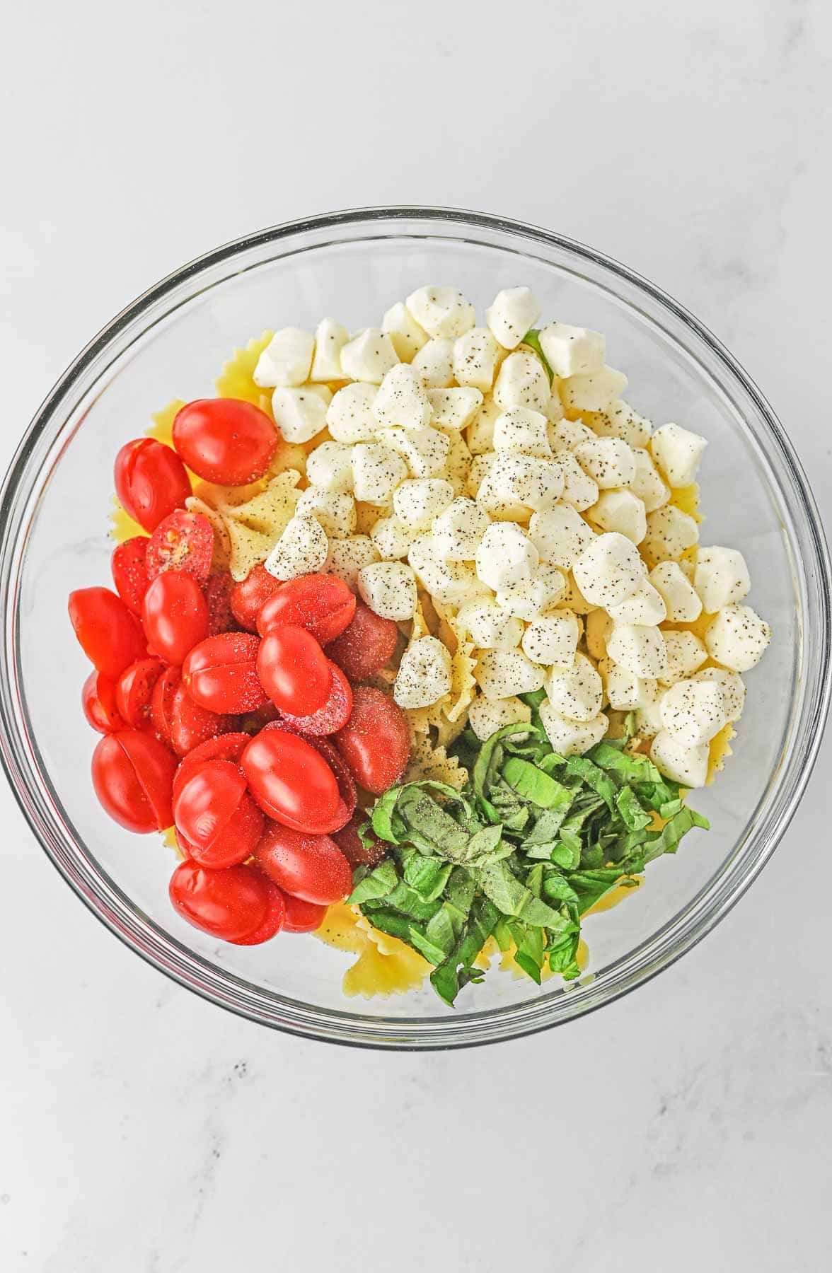 Ingredients for Caprese Pasta Salad in a large glass mixing bowl.