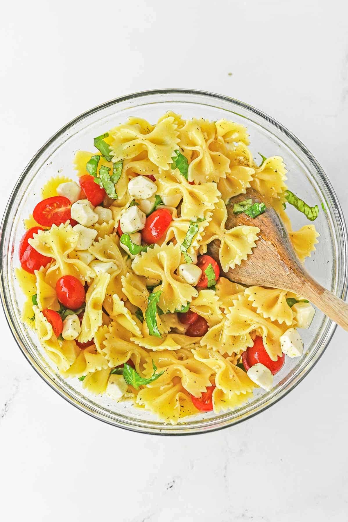 Caprese Pasta Salad in a large glass mixing bowl with wooden spoon.