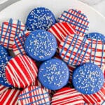 Multiple patriotic red white and blue dipped oreos stacked on a large white plate.