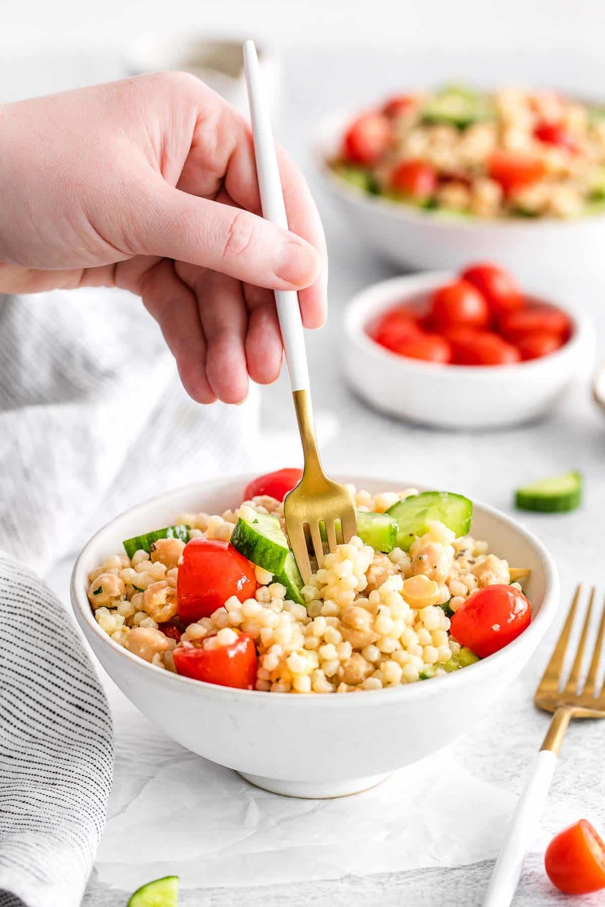 Mediterranean couscous salad in white bowl with fork inserted by womans hand.