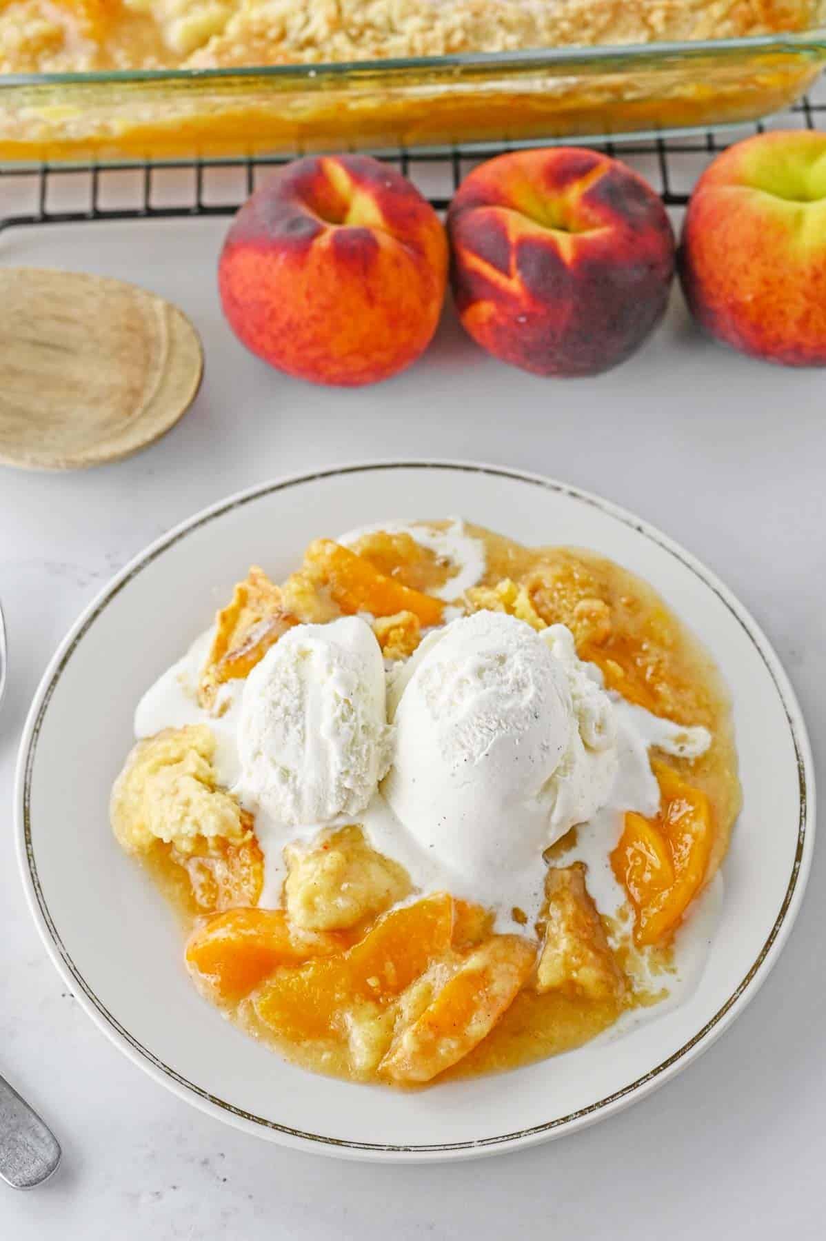 Peach dump cake with a scoop of vanilla ice cream on a white plate.