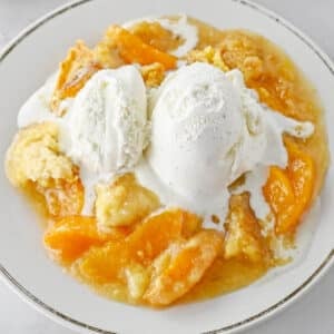 Peach dump cake with a scoop of vanilla ice cream on a white plate.