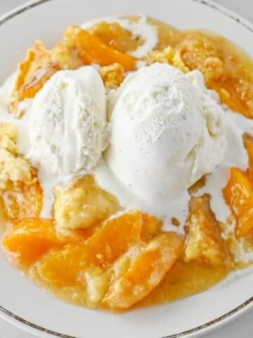 Peach dump cake with a scoop of vanilla ice cream on a white plate.