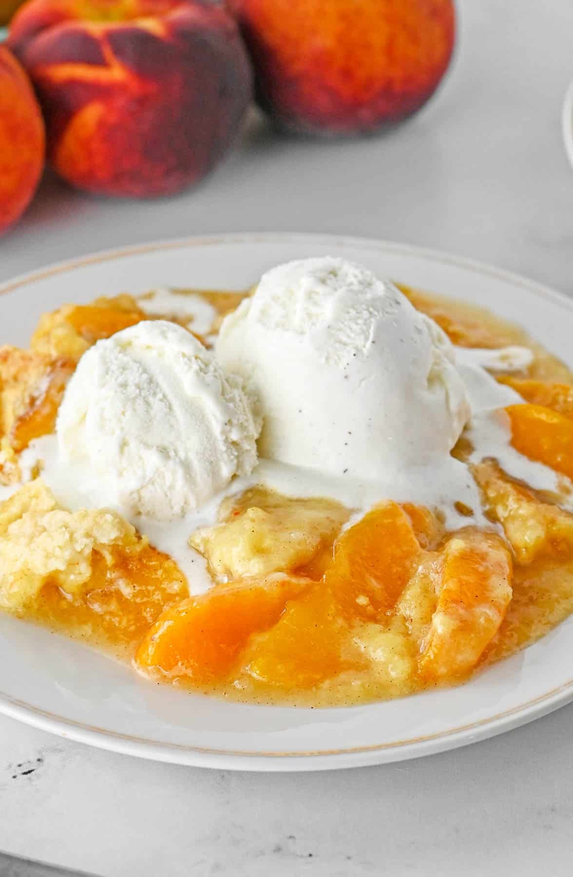 Close up of peach dump cake with a scoop of vanilla ice cream on a white plate.