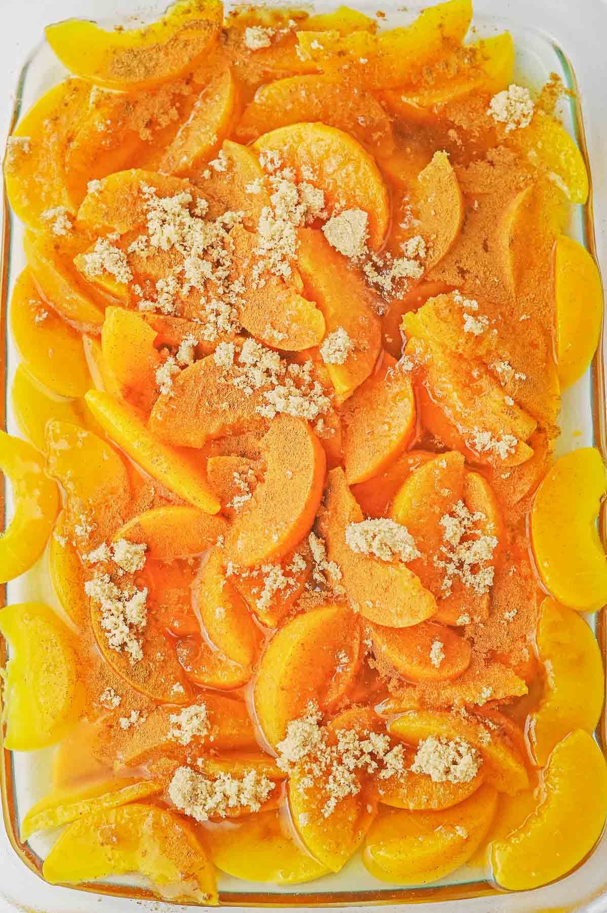 Brown sugar spread over peaches in glass baking dish.