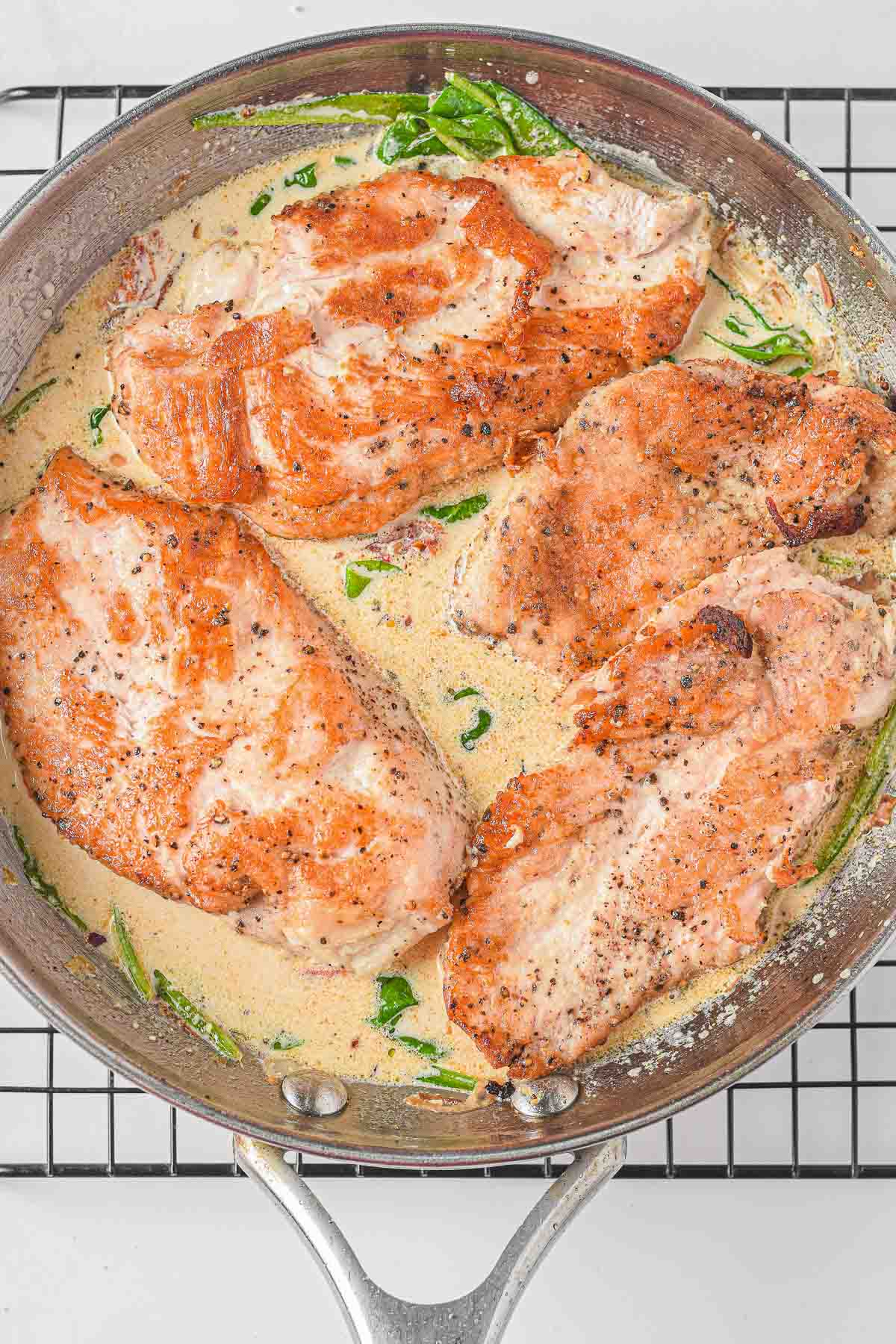 silver skillet with four chicken cutlets in a cream sauce.