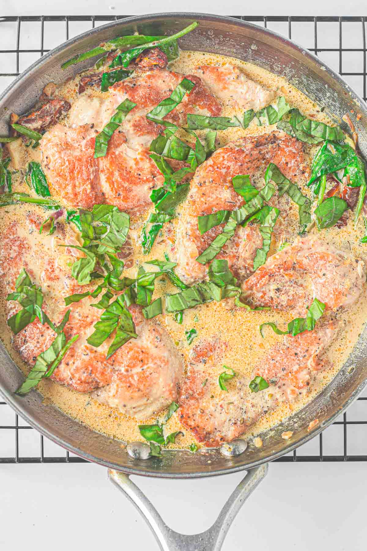 stainless steel skillet full of a tuscan chicken recipe with sun-dried tomatoes, spinach in a creamy sauce.