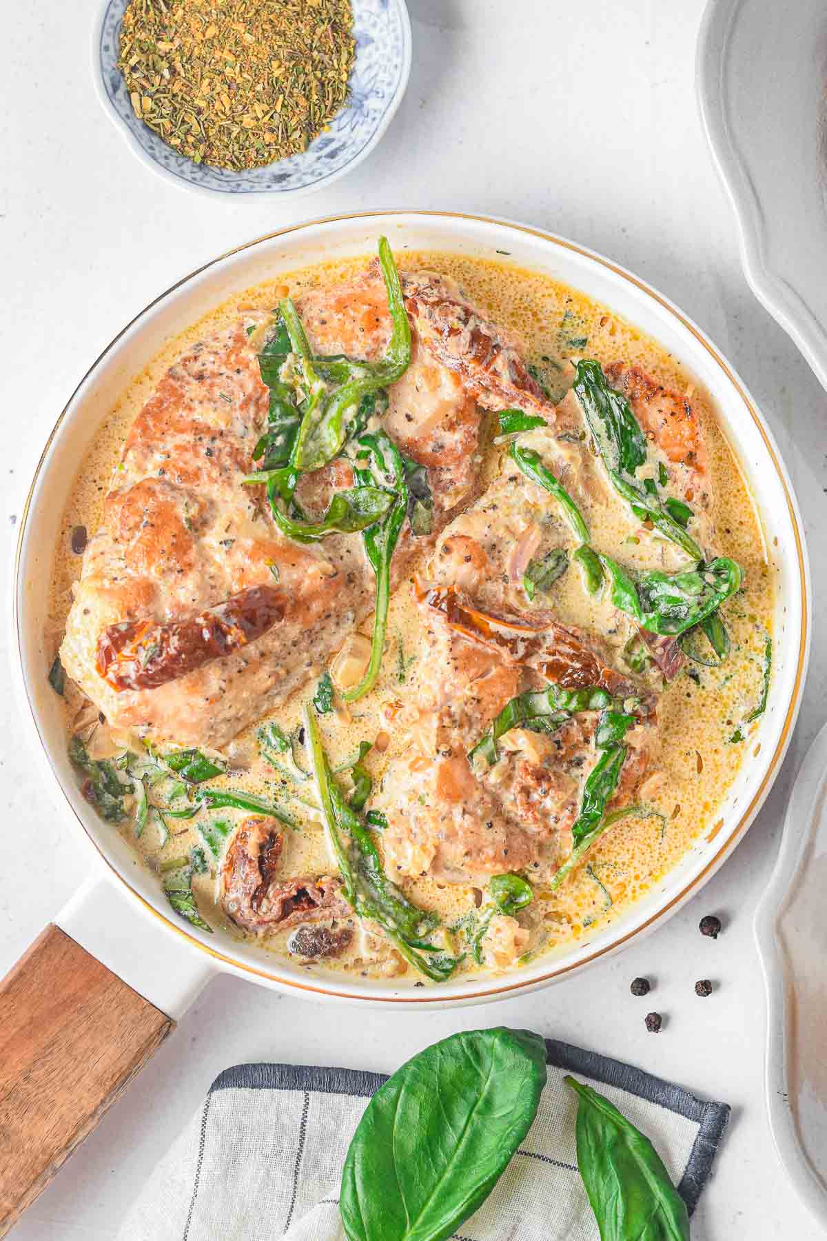 White skillet with tuscan chicken recipe with sun-dried tomatoes, spinach in a creamy sauce.
