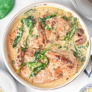 White skillet with tuscan chicken recipe with sun-dried tomatoes, spinach in a creamy sauce.