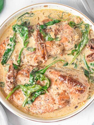 White skillet with tuscan chicken recipe with sun-dried tomatoes, spinach in a creamy sauce.