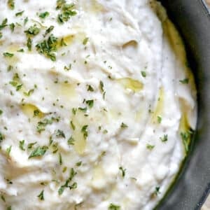 closeup of white bean dip topped with parsley in a black bowl
