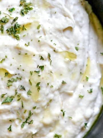 closeup of white bean dip topped with parsley in a black bowl