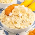 white bowl full of banana pudding fluff topped with vanilla wafers,sliced bananas and mini marshmallows.