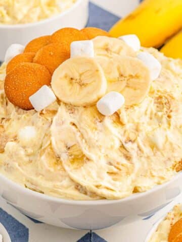 white bowl full of banana pudding fluff topped with vanilla wafers,sliced bananas and mini marshmallows.