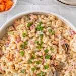 Macaroni Salad in white bowl with a silver serving spoon.