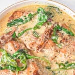 White bowl of creamy tuscan chicken recipe with spinach and sun-dried tomatoes in a creamy sauce.