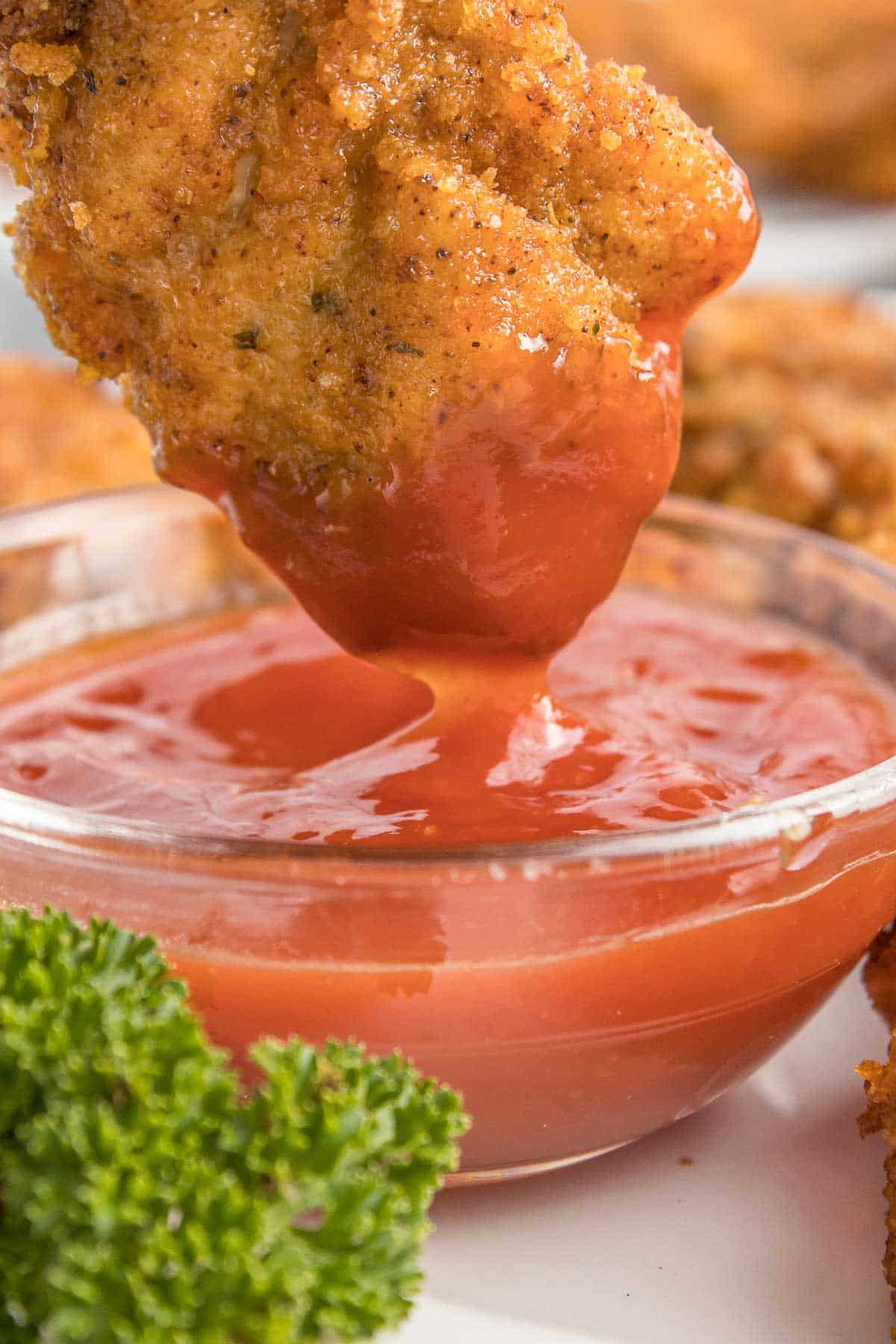 A chicken nugget being dipped into a small glass bowl of ketchup.