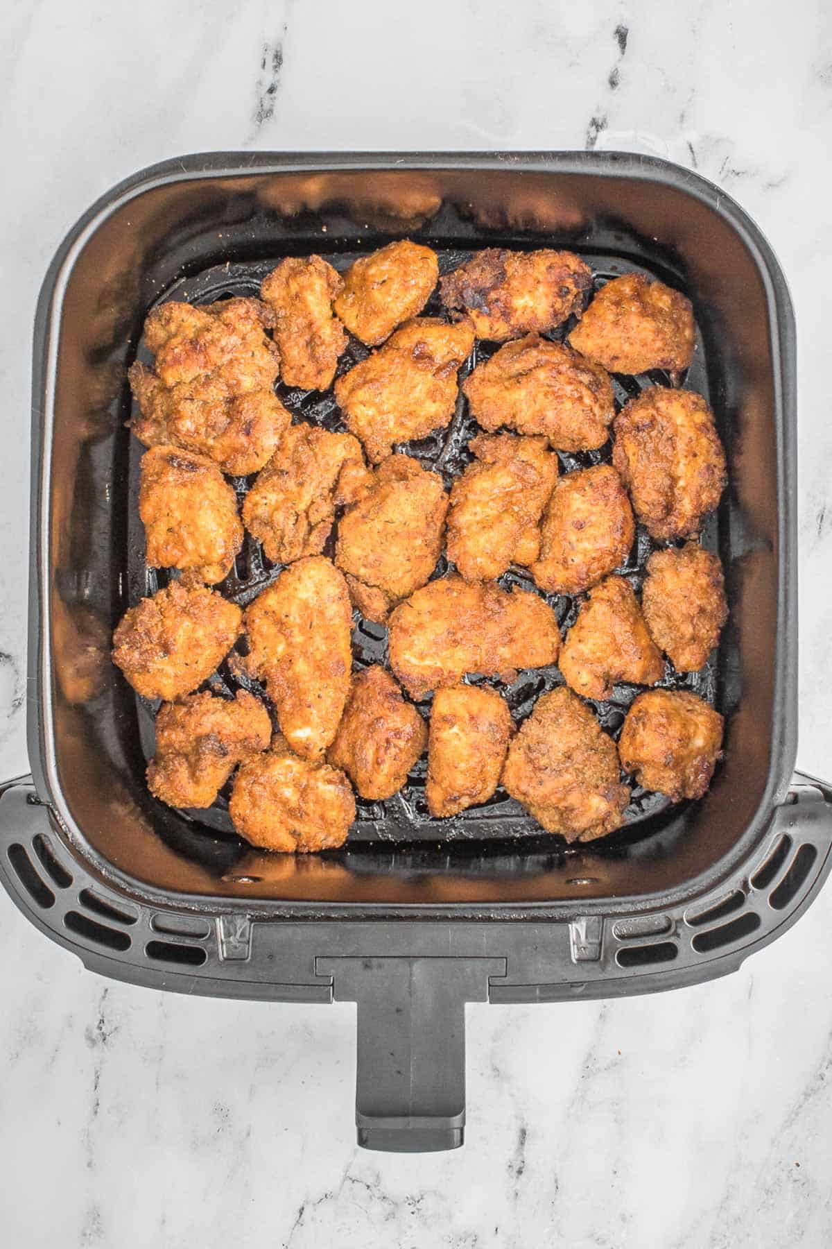 Fried chicken nuggets in bottom of air fryer.