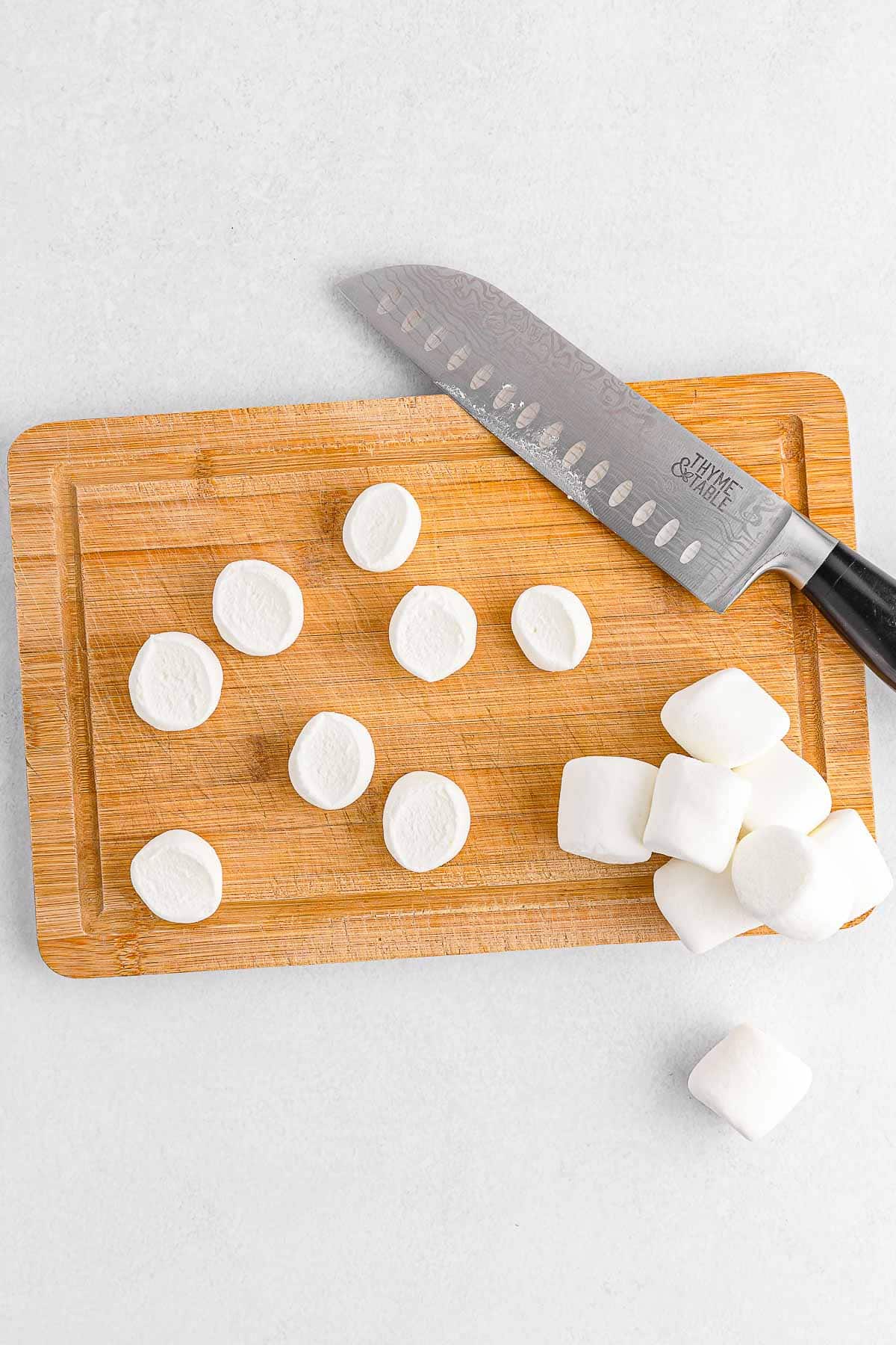 Marshmallows on cutting board being sliced in half prior to cooking in air fryer.