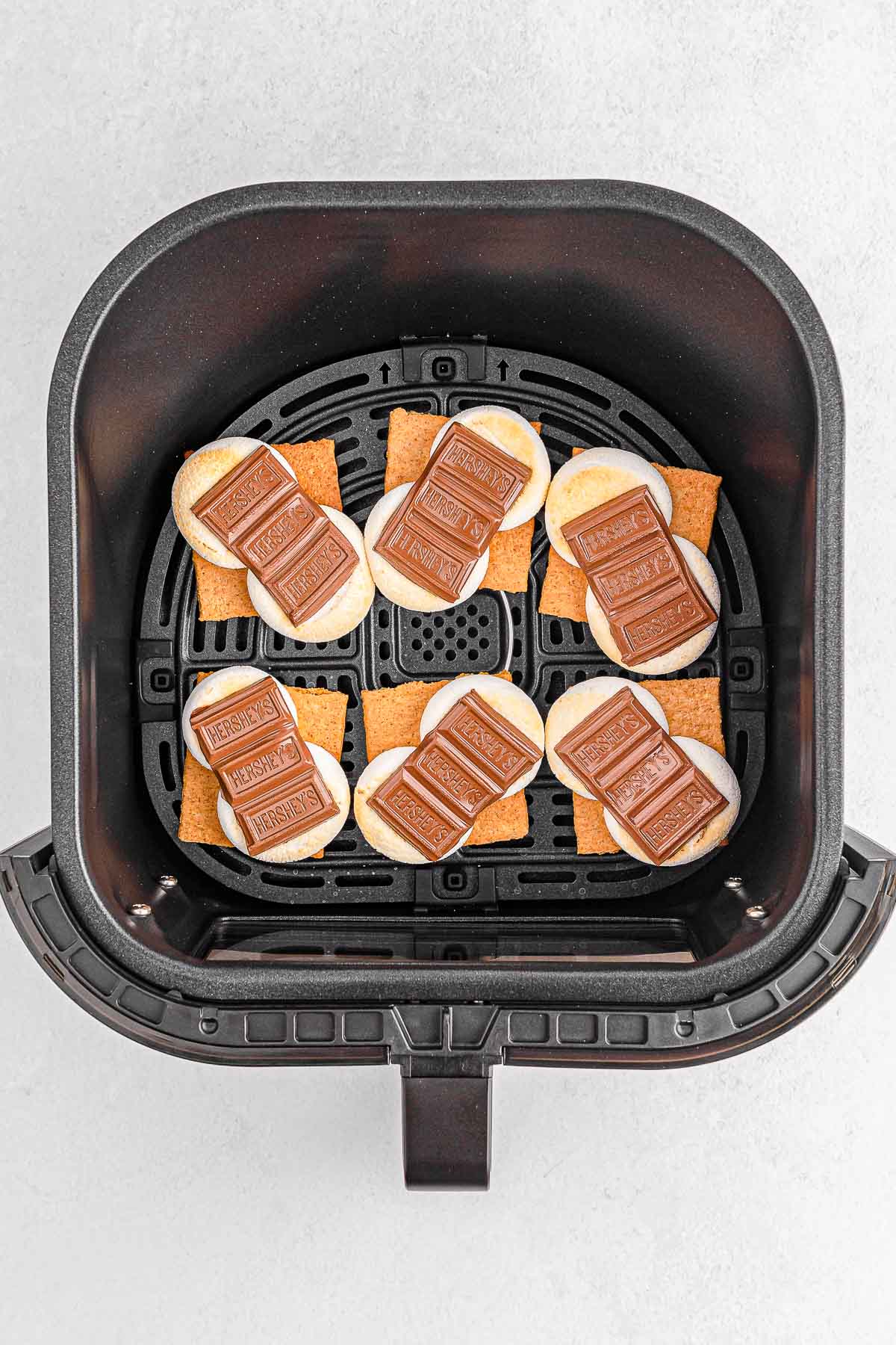 Six cooked smores in air fryer with melted chocolate.