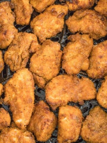 several crispy chicken nuggets in bottom of air fryer basket.