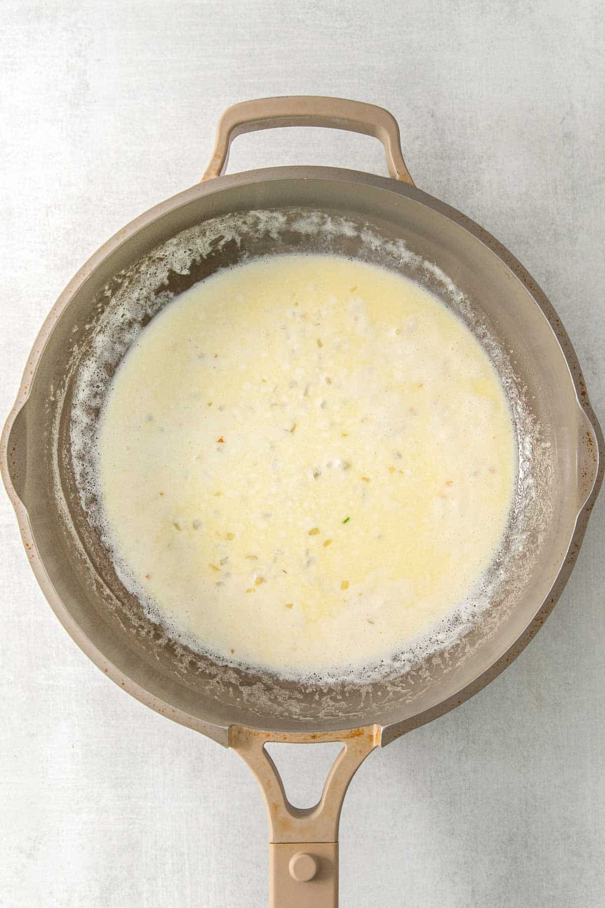 Heavy cream and minced garlic and parmesan cheese added to butter mixture in saucepan.