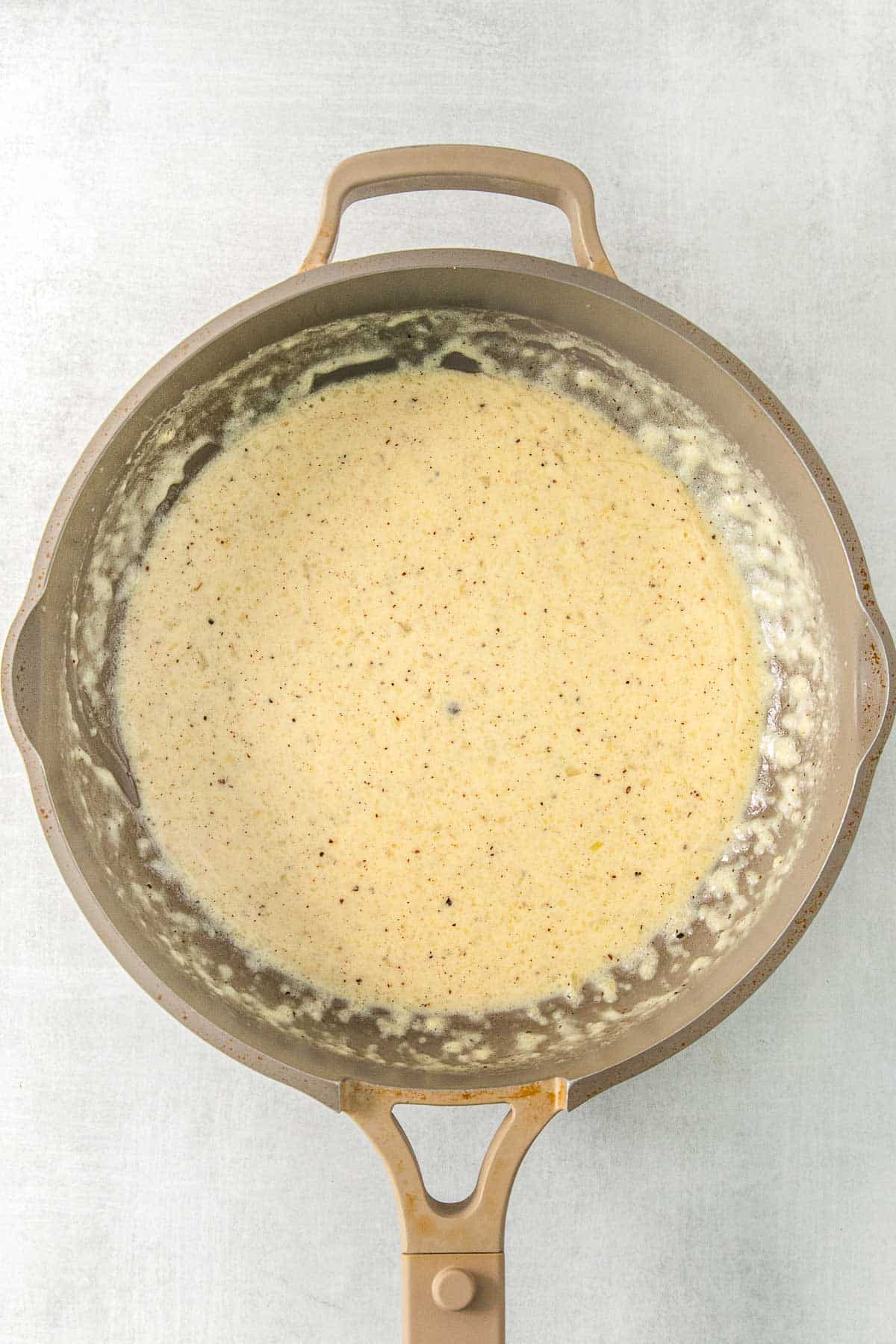Pepper, nutmeg, and salt added to sauce mixture in saucepan.