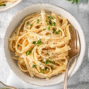 Alfredo sauce poured over white bowl of pasta.