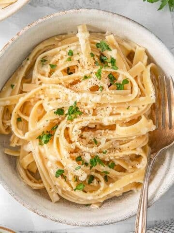 Alfredo sauce poured over white bowl of pasta.