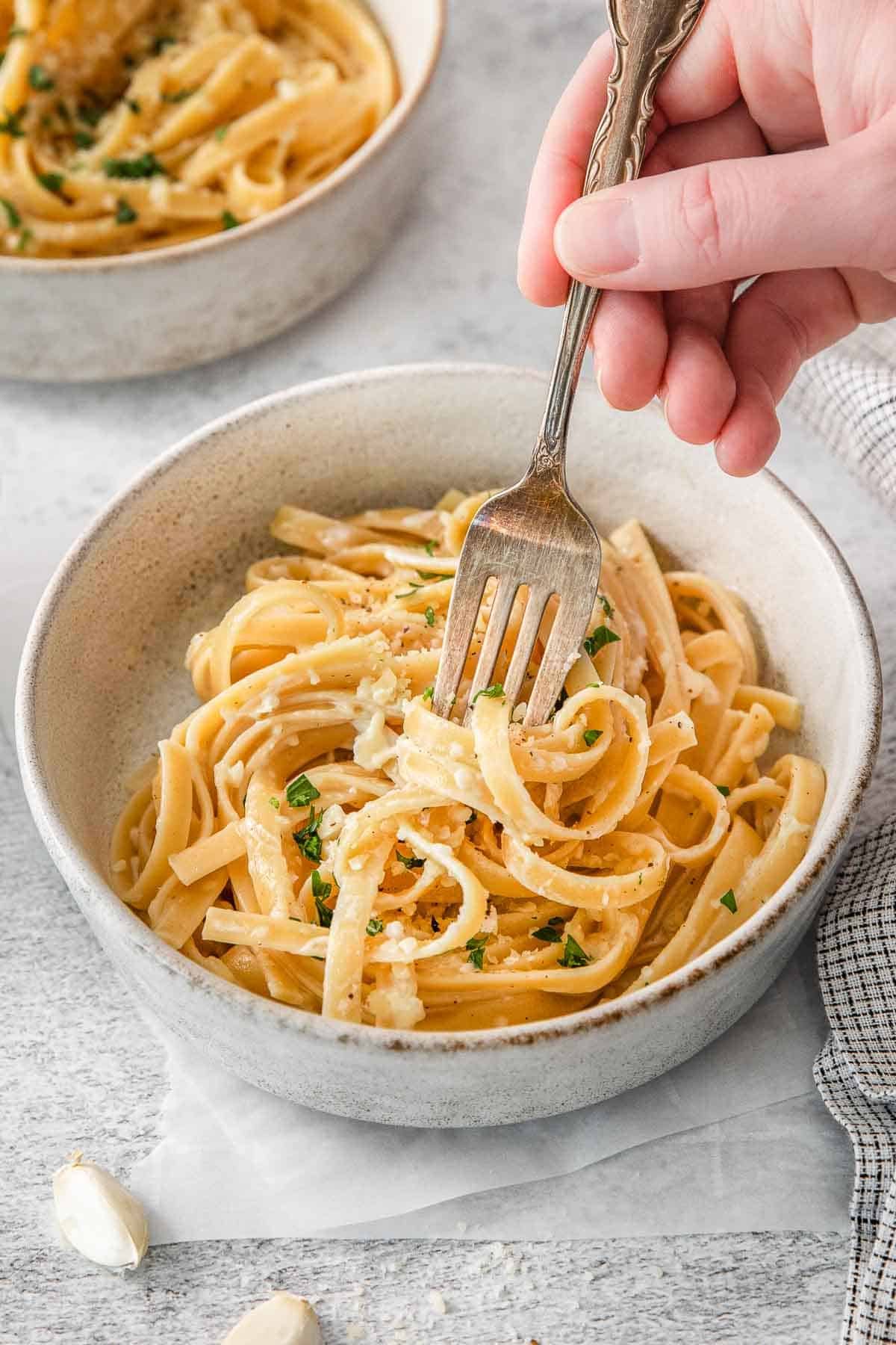 Alfredo sauce poured over white bowl of pasta with fork inserted.