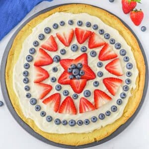 Fruit pizza on pizza pan topped with strawberries and blueberries.