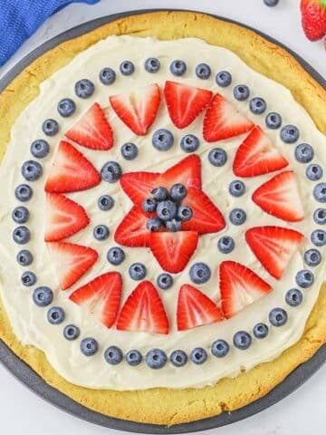 Fruit pizza on pizza pan topped with strawberries and blueberries.