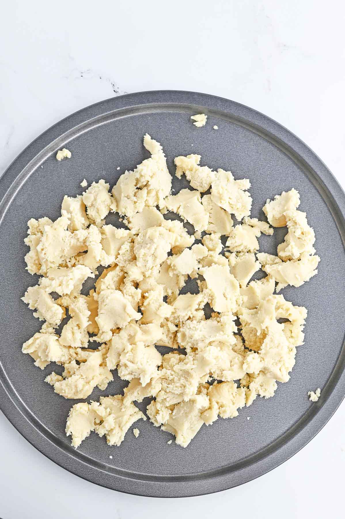 Sugar cookie dough crumbled over pizza pan.