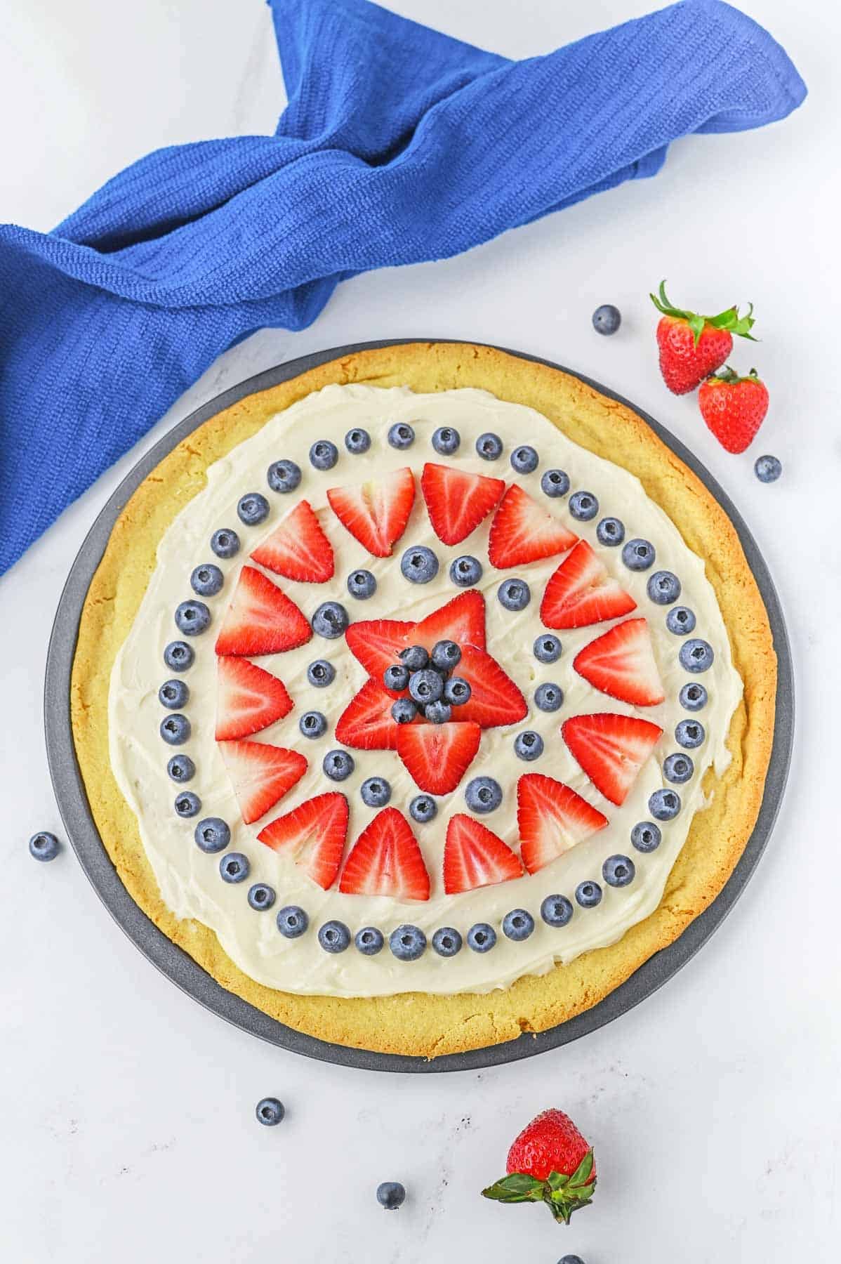 Fruit pizza on pizza pan topped with strawberries and blueberries.