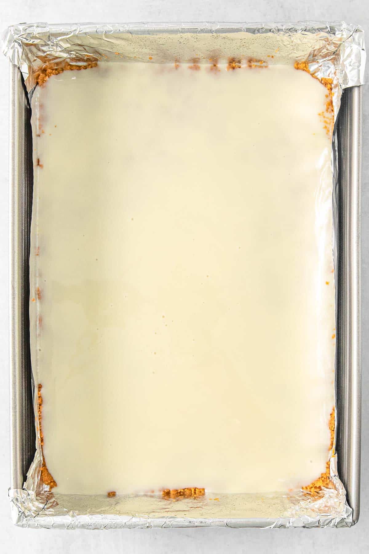 Sweetened condensed milk evenly poured over the graham cracker crust in baking sheet.