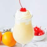 Orange shake topped with whip cream and cherry in a tall glass.