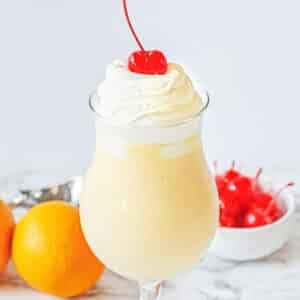 Orange shake topped with whip cream and cherry in a tall glass.