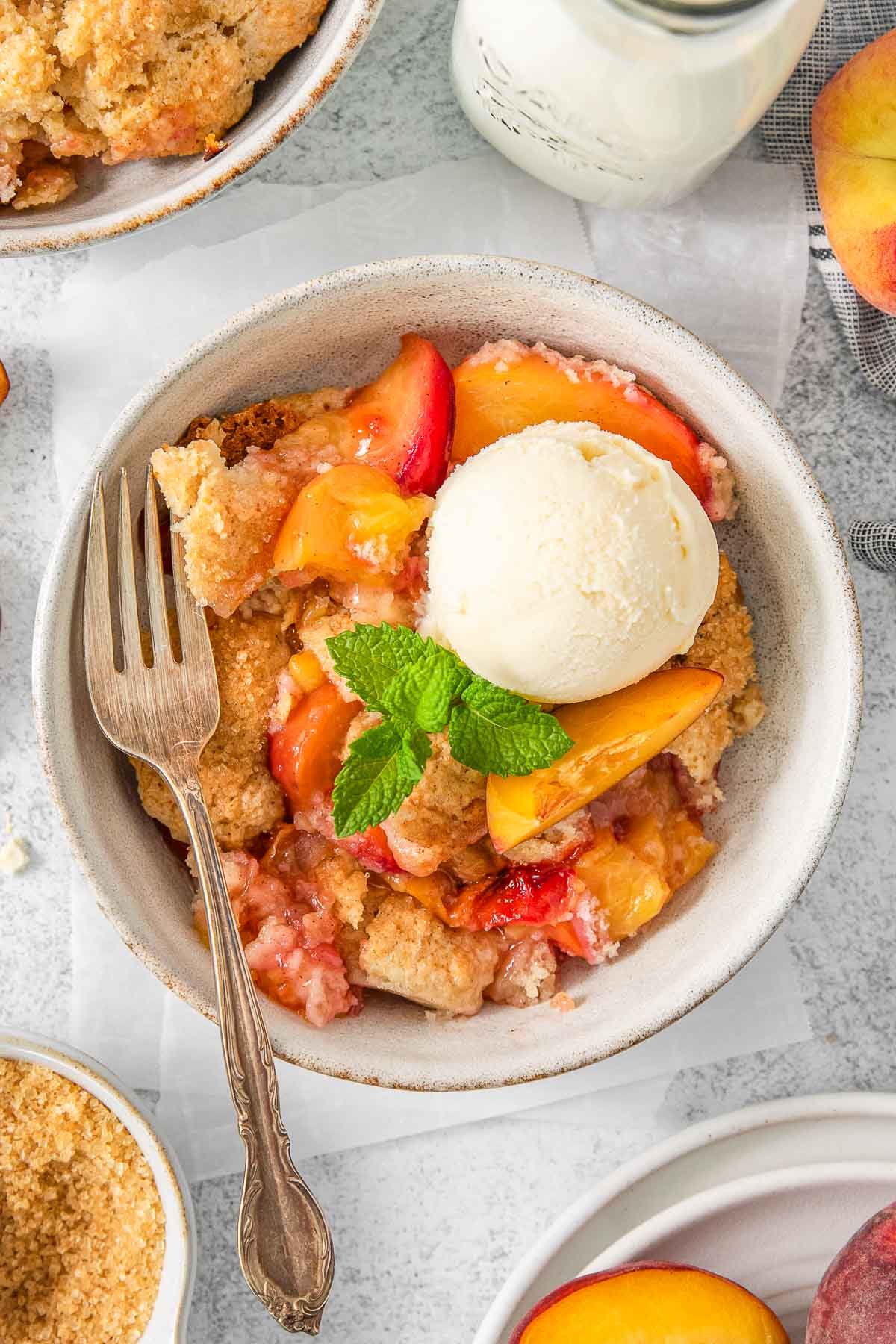 Peach cobbler in a white bowl topped with ice cream.