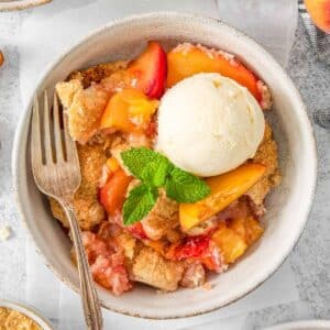 Peach cobbler in a white bowl topped with ice cream.