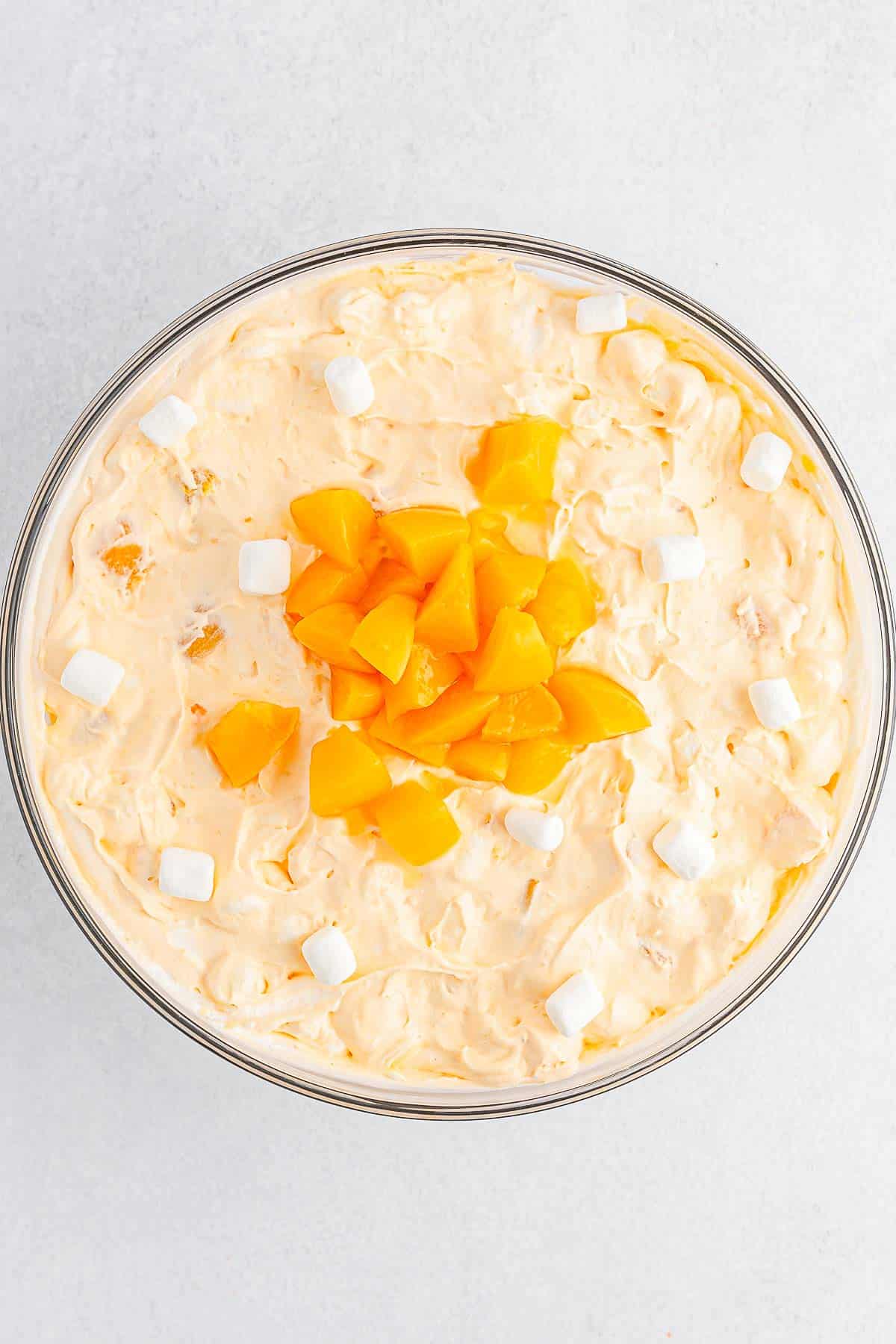 Large glass mixing bowl of Peach Fluff with peaches and marshmallows.