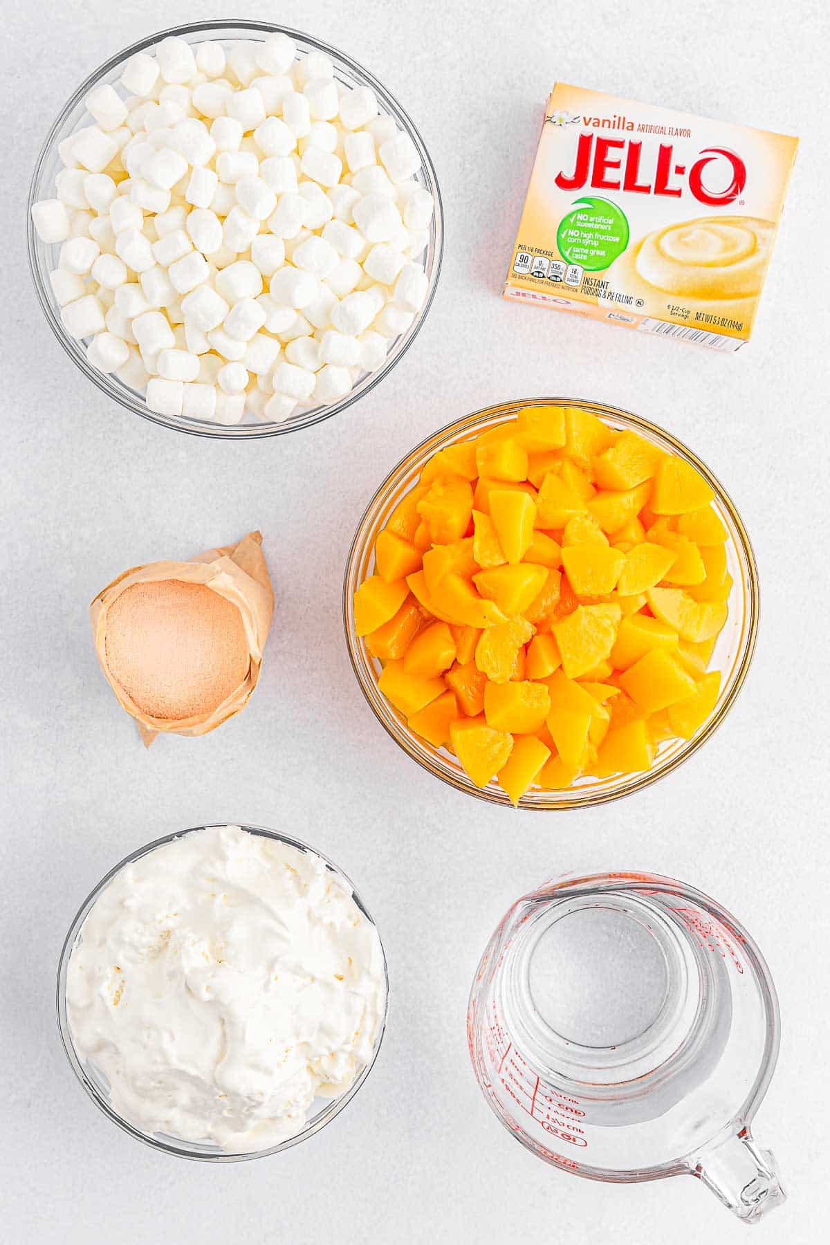 Several bowls of ingredients for Peach Fluff - Peach Jell-O mix, hot water, cold water, instant vanilla pudding, cool whip, sliced peaches, mini marshmallows.