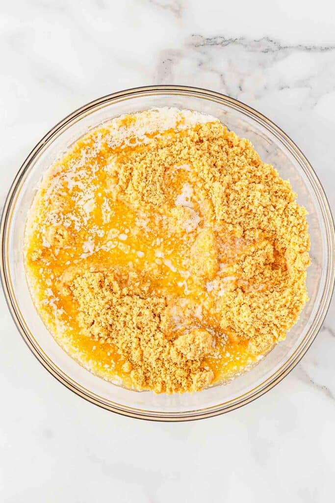 Golden oreo breadcrumb and butter combined in glass mixing bowl.