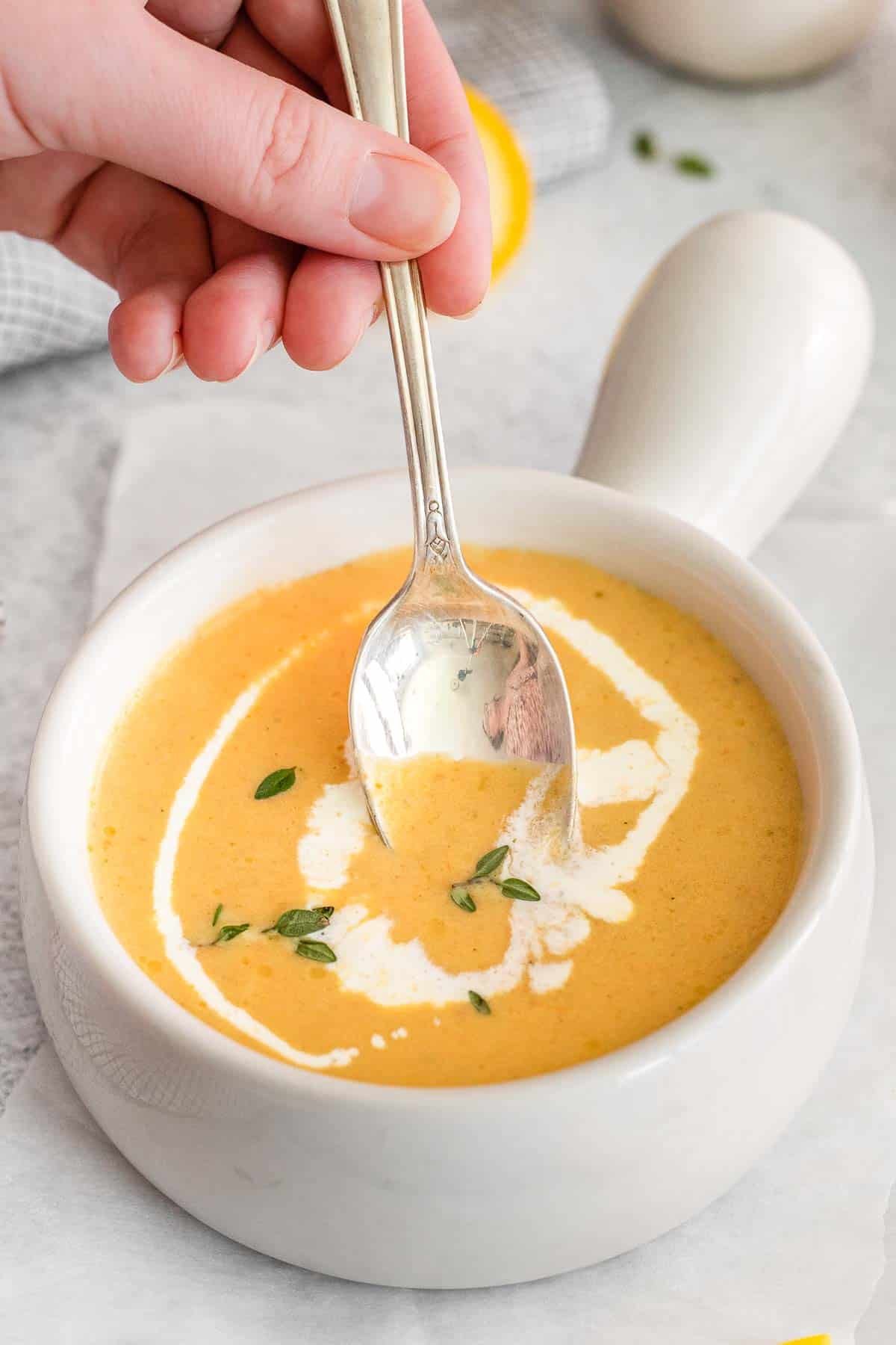 Yellow squash soup in a small white bowl with hand holding spoon in the soup.